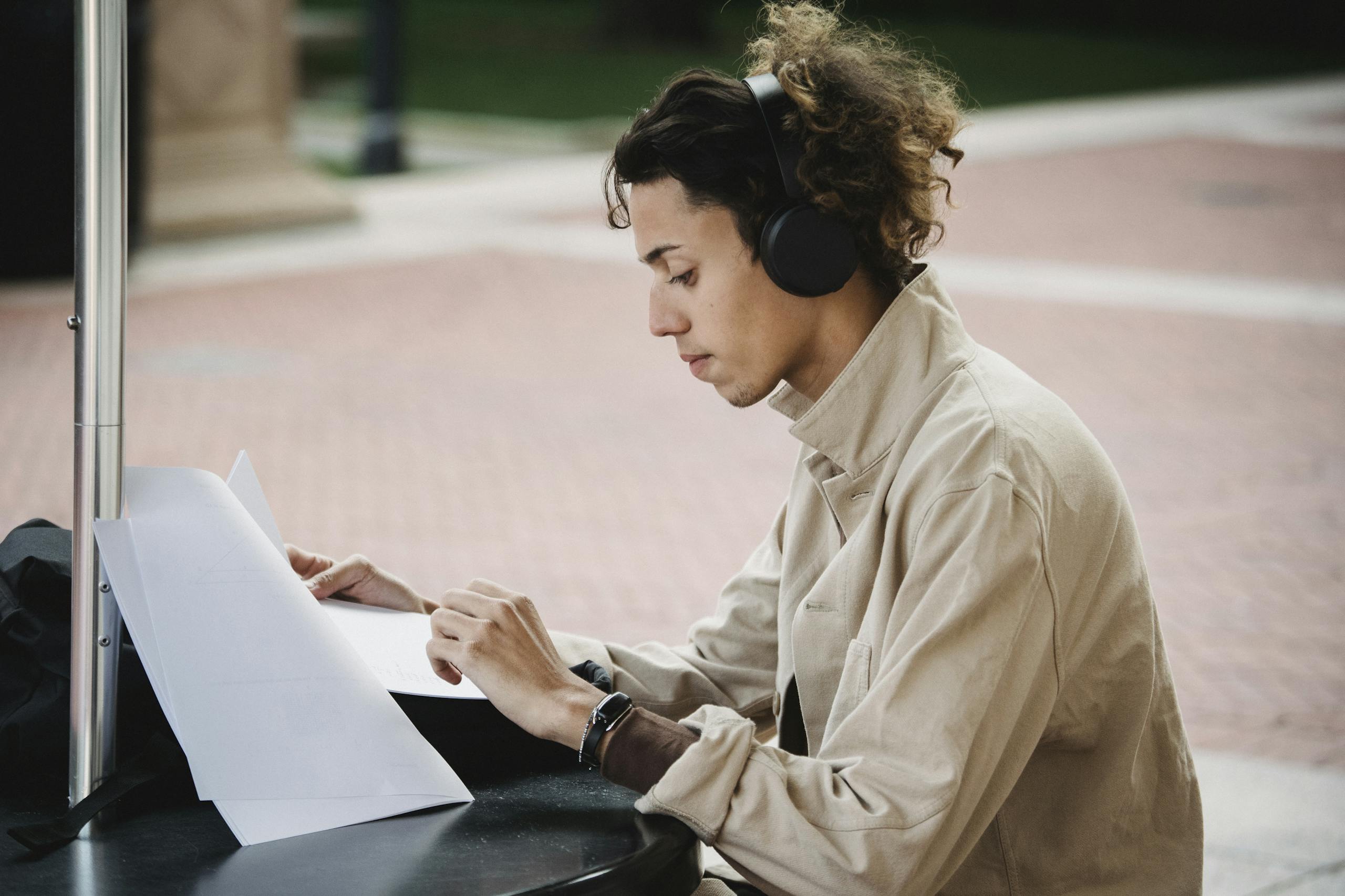 Side view of concentrated male learner preparing report for university assignment while listening to music in wireless headphones